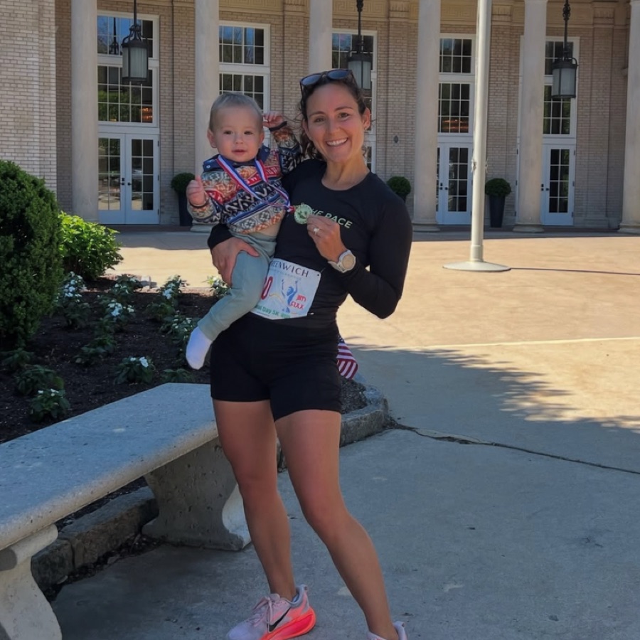 KTP runner in club kit with medal, holding a toddler, after a 5K